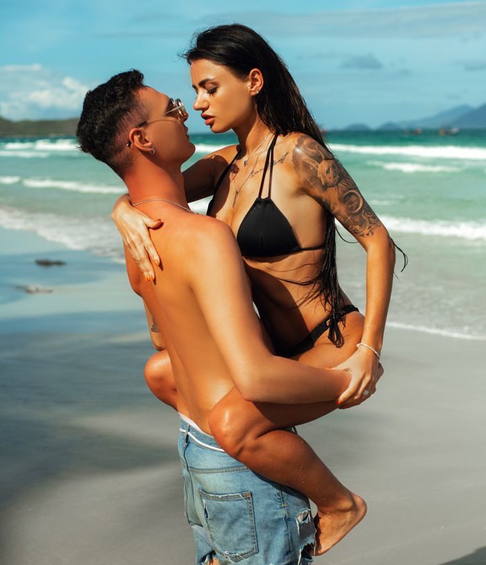 A couple shares a romantic moment on a sunny tropical beach with clear blue waters.